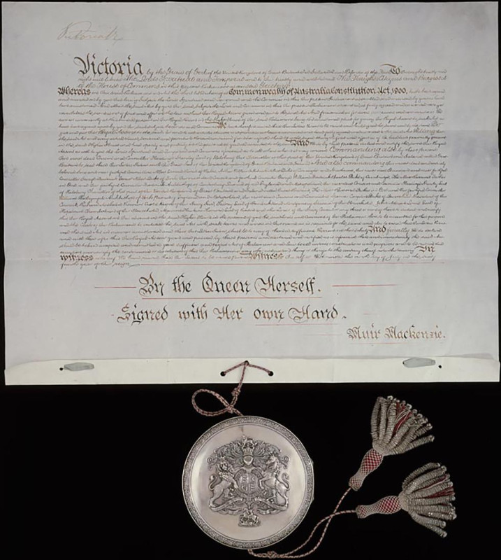 An old document with a large amount of neatly handwritten decorative text. A round silver case is attached to the bottom of the document by a red and silver cord. Two silver and red tassels hand from the silver case.