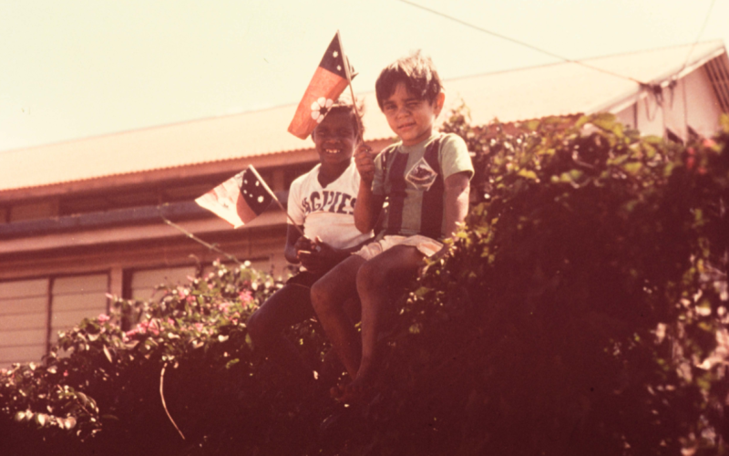 2 boys sit together waving an orange and black flag.