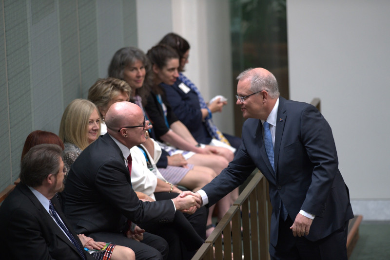 A man in a suit leans over a railing to shake hands with a group of people.