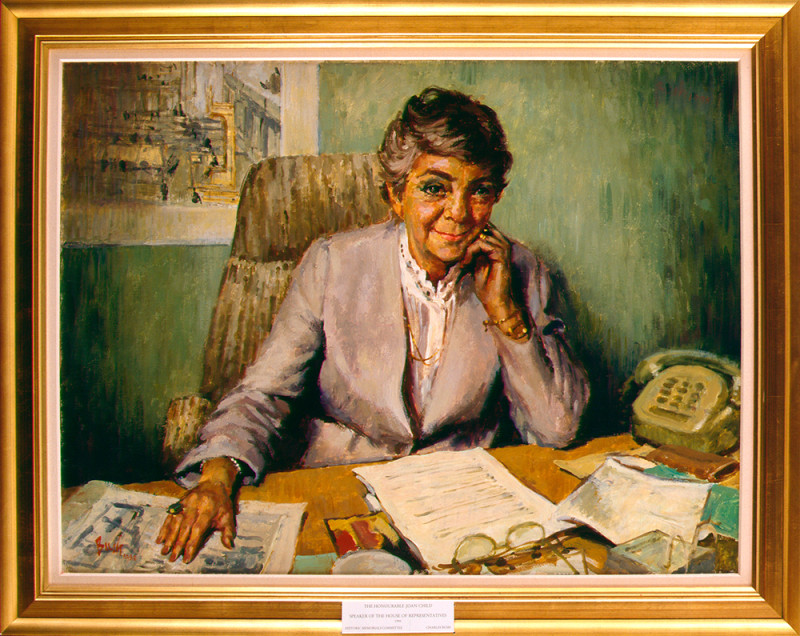 An oil painting of a woman with a smile on her face, sitting at a desk. The desk has various papers, a pair of glasses and a telephone on it.