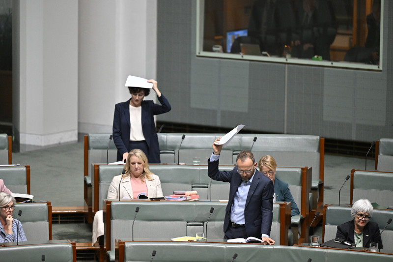 Members of the House of Representatives stand while holding a piece of paper above their heads.