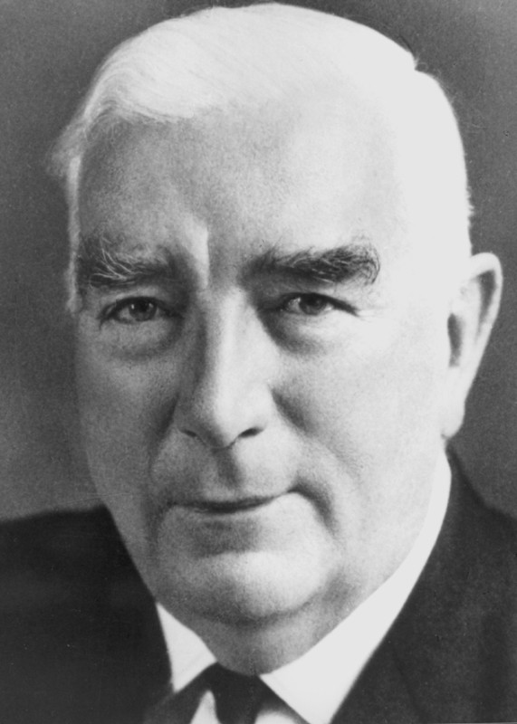 A black and white photographic portrait of a man with white hair wearing a suit and tie.