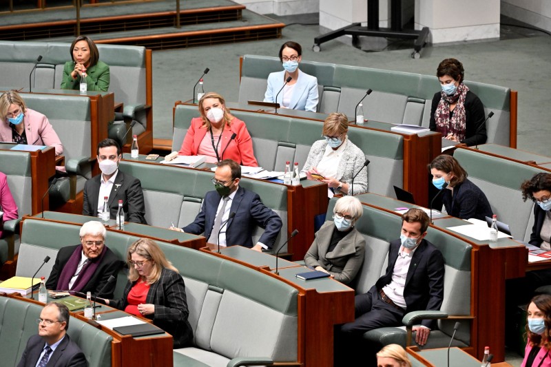 Men and women sit on green benches with desks. They are listening and working on their devices.