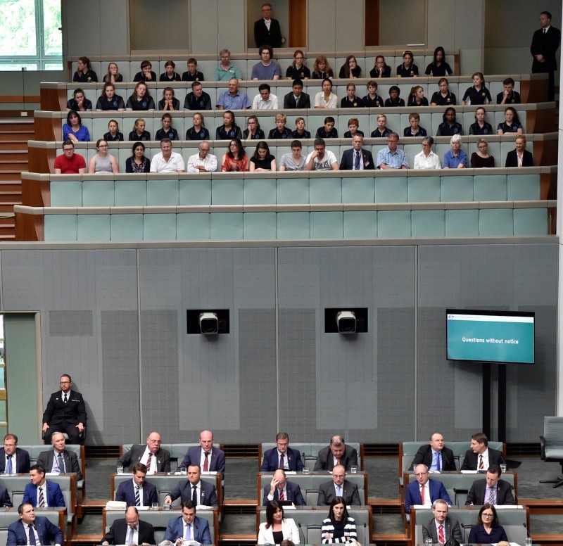 People sitting in rows of benches above other people sitting in rows in the green House of Representatives.