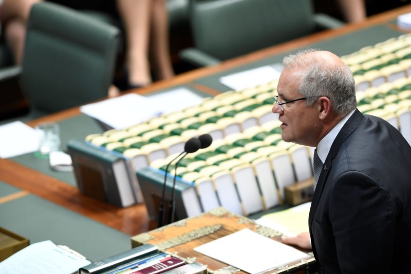 A man in a suit stands at a large wooden table. In the centre are rows of books lined up with the spines up. The books are bound in green and cream binding.